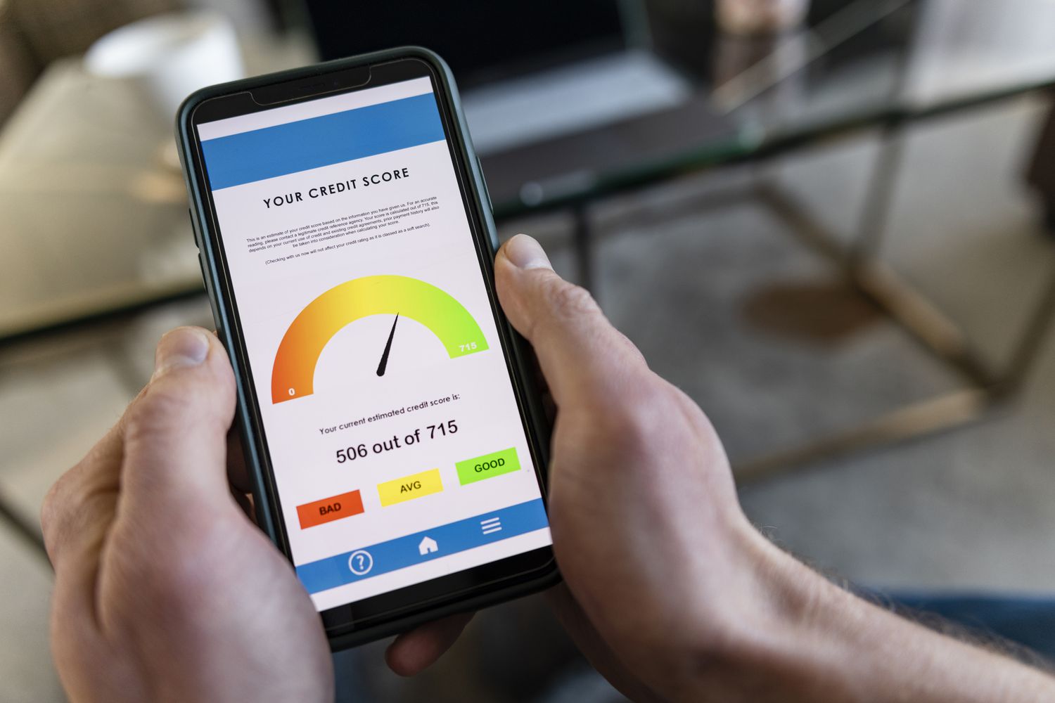 Person holding a smartphone displaying a credit score monitoring app with a gauge reading
