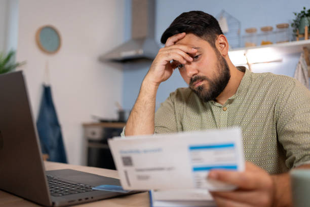 A man stressed while reviewing financial documents and bills at his kitchen table